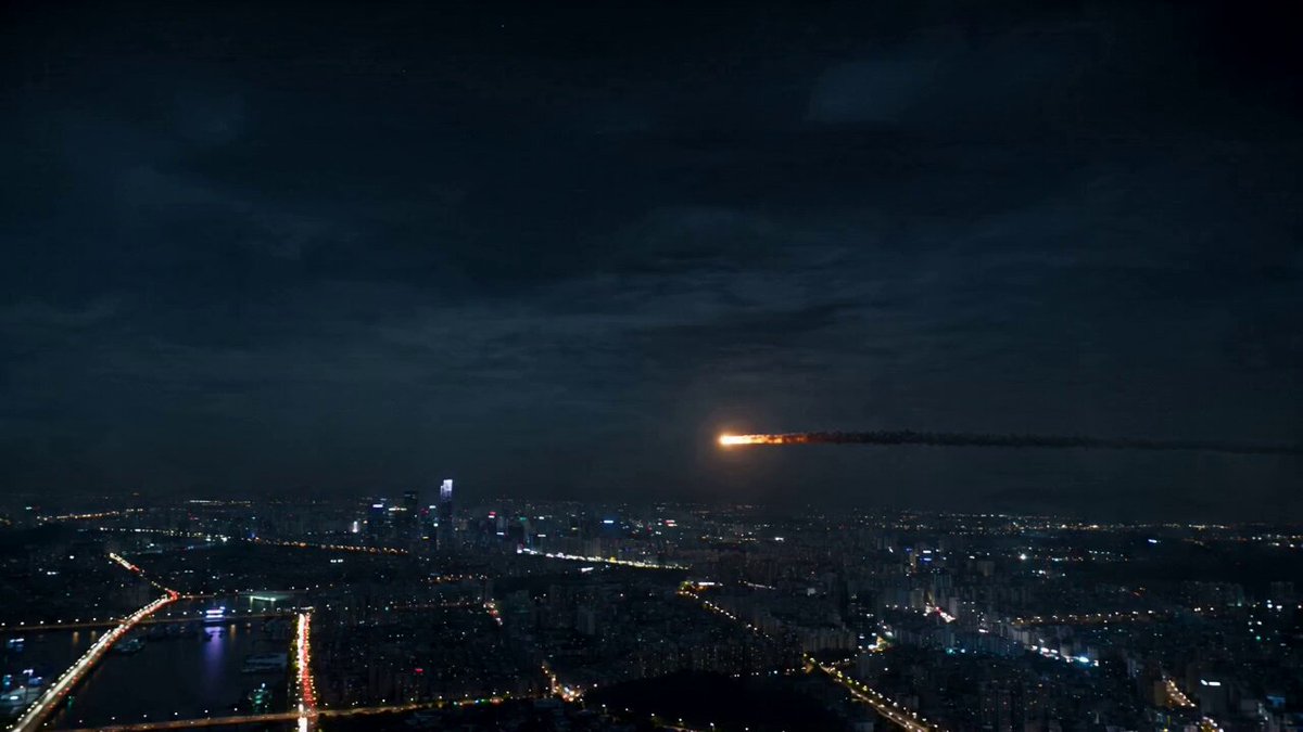 A glowing asteroid enters the atmosphere above a sprawling metropolis at night.