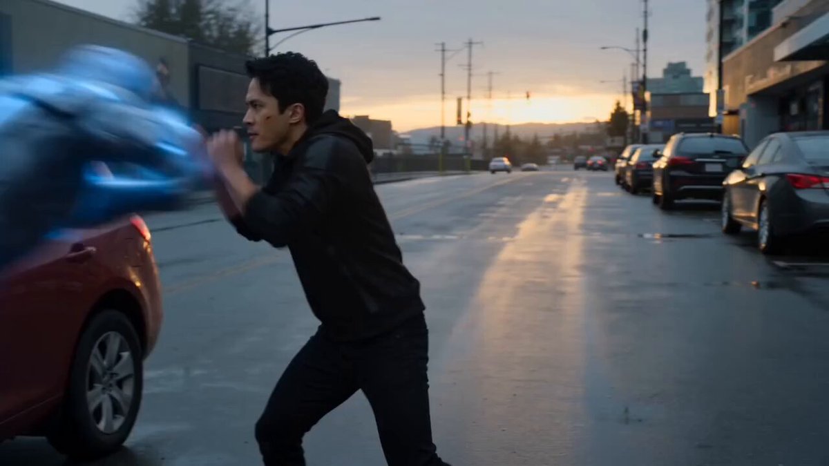 An intense, cinematic, slow-motion action sequence on a damp, overcast city street during dusk. 